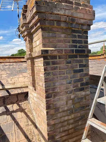 Freshly repointed brick chimney stack with ladder on the roof