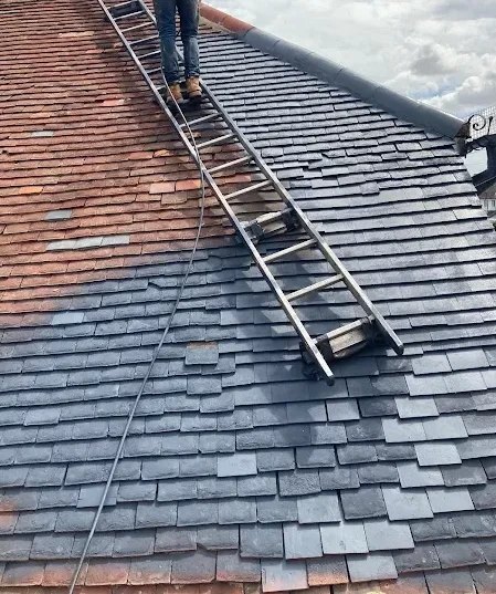 Roof Spraying: Roofer on a ladder spraying a slate roof in Kent