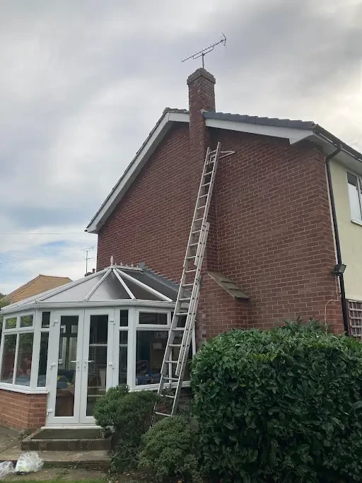 Ladder up to a brick chimney on a gable end beside a conservatory