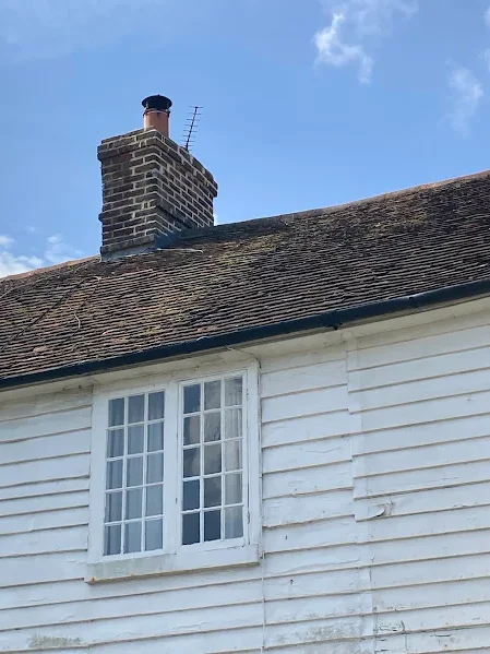 Brick chimney on a weatherboarded cottage roof before chimney work