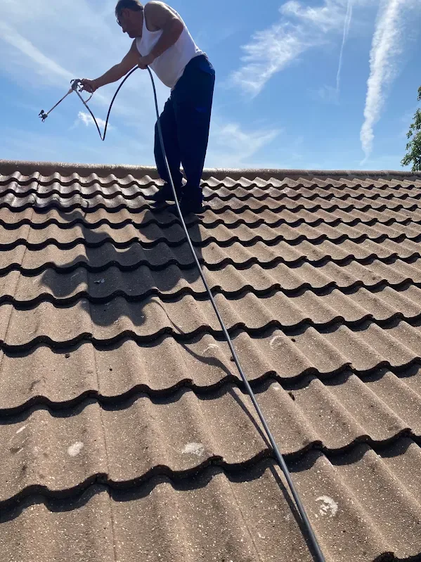 Roofer spraying a concrete tiled roof on a sunny day